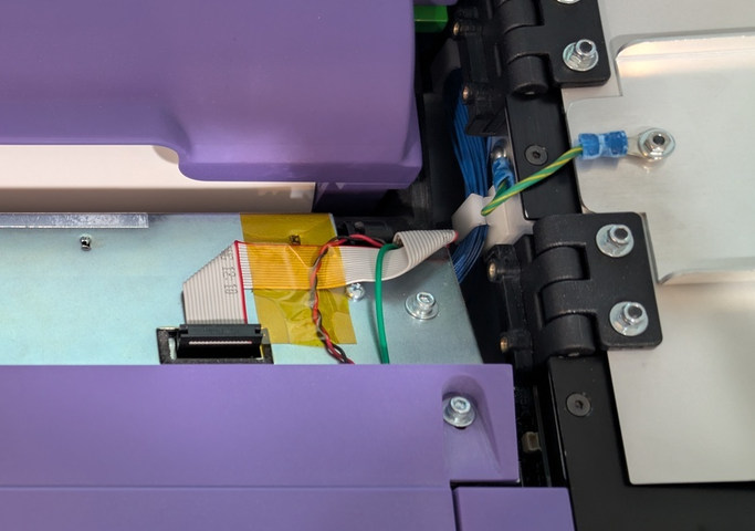Photo of cables seen after opening scanner access door.  From left to right on the scanner metal: ribbon cable, twisted pair of wires, and a single wire. On the far right: another single wire connected to the scanner access door.